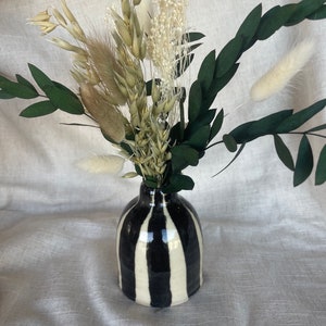 May include: A small, black and white striped ceramic vase containing a bouquet of dried flowers, including white pampas grass, oat stalks, and small white flowers.