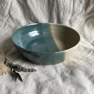 May include: A large, round ceramic bowl with a light blue and white glaze. The bowl has a slightly textured surface and is perfect for serving salads, pasta, or other dishes.