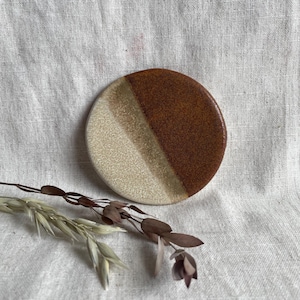 May include: A round ceramic dish with a white and brown glaze. The dish is slightly raised in the center and has a smooth, glossy finish.