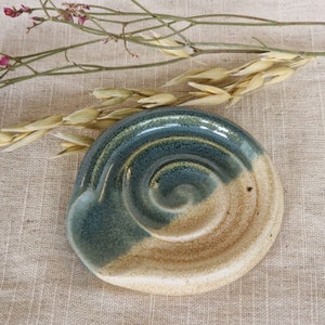 May include: A ceramic dish with a swirl design in shades of blue and beige. The dish has a textured surface and a slightly raised rim.