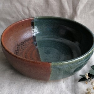 May include: A large, ceramic bowl with a brown and green glaze. The bowl is divided in half, with one side being a deep brown and the other side being a dark green.