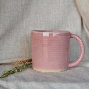 May include: A pink ceramic mug with a slightly textured surface and a rounded handle.