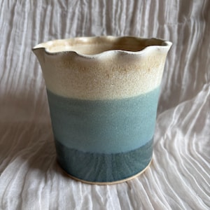 May include: A ceramic plant pot with a wavy rim, showcasing a colour gradient. The top is light beige, fading into teal blue, and finishing with a darker blue at the base. Suitable for indoor plants, it is likely handmade.