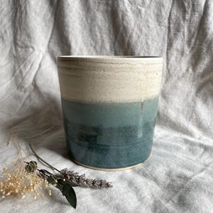 May include: A ceramic planter with a white top and a blue bottom. The planter has a speckled glaze and a rounded shape.