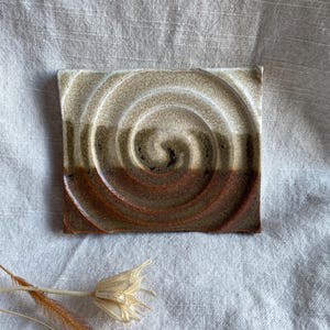Peut inclure: Un carreau de céramique carré avec un motif en spirale brun, vert et blanc. Le carreau a une surface texturée.