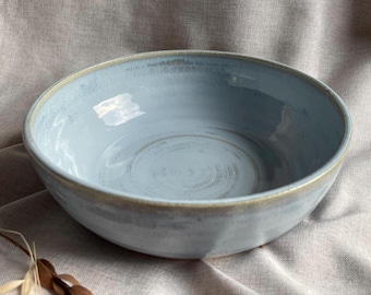 May include: A light blue ceramic bowl with a slightly textured surface. The bowl is empty and has a subtle, faded look.