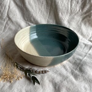 May include: A large, white and blue ceramic bowl with a speckled glaze. The bowl is sitting on a white fabric surface.