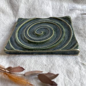 Peut inclure: Un carreau de céramique carré avec un glaçage vert et blanc. Le carreau présente un motif en spirale au centre.