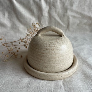 May include: A white ceramic butter dish with a lid and a handle. The dish has a speckled finish.
