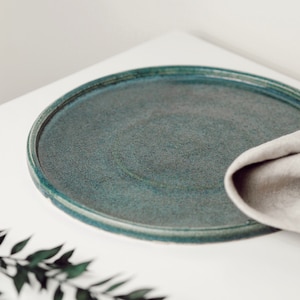 May include: A round, teal ceramic plate with a slightly raised rim. The plate is on a white surface.