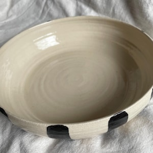 May include: A white ceramic bowl with black polka dots around the rim. The bowl is slightly rounded and has a smooth, glossy finish.