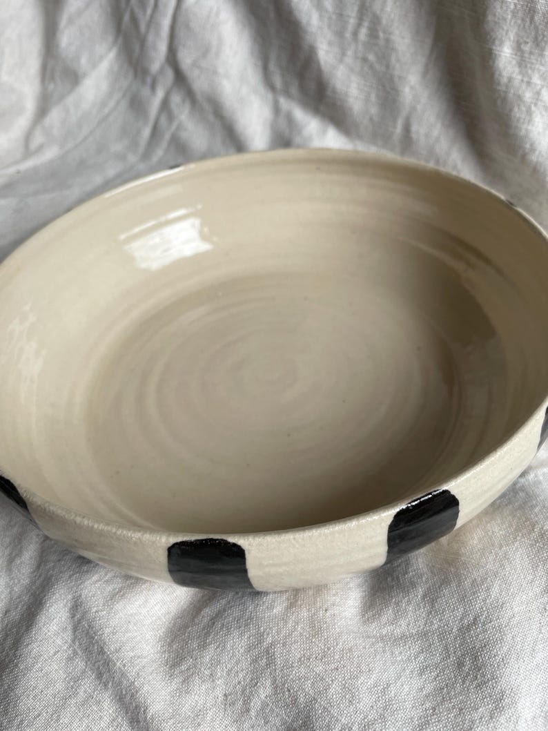 May include: A white ceramic bowl with black polka dots around the rim. The bowl is slightly rounded and has a smooth, glossy finish.