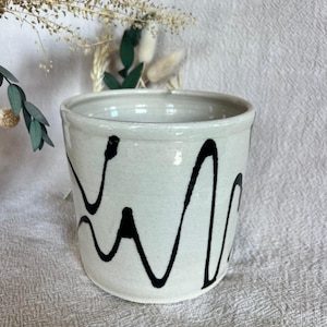 Peut inclure: Un pot de fleurs en céramique avec un glaçage gris clair et des gribouillis noirs abstraits. Le pot cylindrique a une large ouverture et convient aux plantes d'intérieur. La poterie faite à la main a une esthétique rustique et moderne.