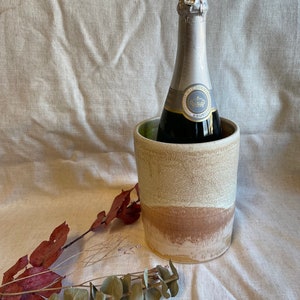 Peut inclure: Un refroidisseur à vin en céramique avec un glaçage brun clair, beige et blanc. Le refroidisseur contient une bouteille de champagne avec une étiquette en feuille d'argent qui indique "BRUT".