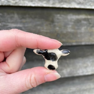May include: A small ceramic cow figurine with black and white spots. The figurine is about the size of a fingertip.