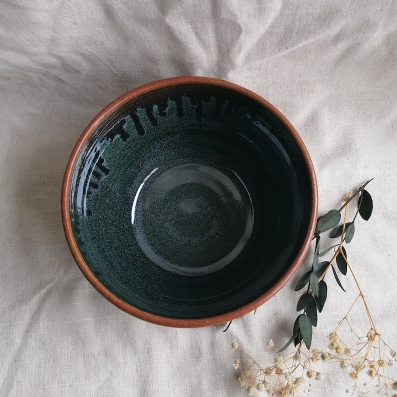 May include: A large, deep bowl with a dark green glaze and a brown rim. The bowl has a speckled, textured surface.