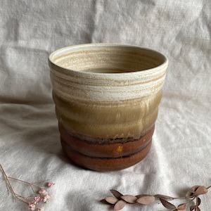 May include: A ceramic planter with a brown, tan, and white glaze. The planter has a rounded shape and a wide opening.