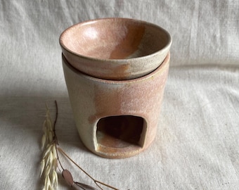 May include: A ceramic essential oil diffuser with a light pink and white glaze. The diffuser has a small opening on the side for a tea light candle.