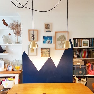 Può includere: Una sala da pranzo con un tavolo e sedie in legno. La parete dietro il tavolo è dipinta di blu con un motivo geometrico. Due lampadari dorati pendono dal soffitto.