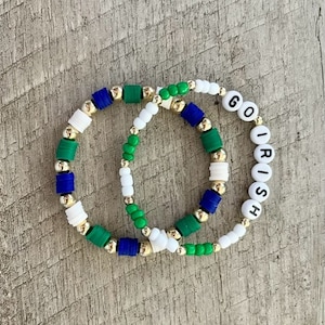May include: Two beaded bracelets with green, white and blue beads. One bracelet has the words "GO IRISH" spelled out in white beads.