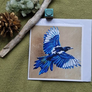Uma pega mágica voa sobre um cartão de felicitações exclusivo. De uma pintura acrílica original de Jane Stewart.