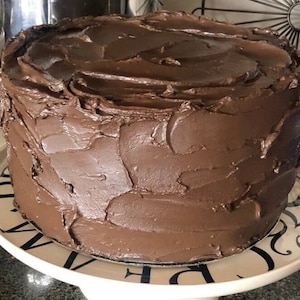 Puede incluir: Un pastel de chocolate cubierto con una gruesa capa de glaseado de chocolate. El glaseado tiene un aspecto de remolino y texturado.