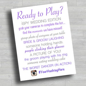 May include: A printable wedding game card with purple text that says "Ready to Play? iSpy Wedding Edition" and lists a series of wedding-themed photo challenges for guests to complete. The card also includes a hashtag for the wedding.