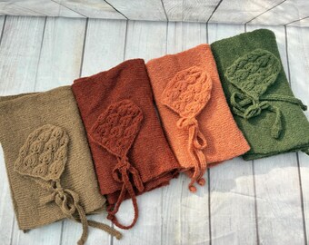 May include: Four sets of knitted baby blankets and matching bonnets in tan, rust, orange, and olive green. Each bonnet features a textured cable knit pattern and long ties. The blankets are made of a simple stockinette stitch fabric.