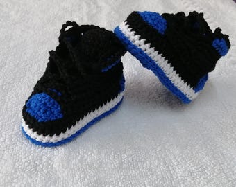 May include: A pair of crocheted baby shoes in black, white, and blue. The shoes have a high-top style with laces and a white sole.