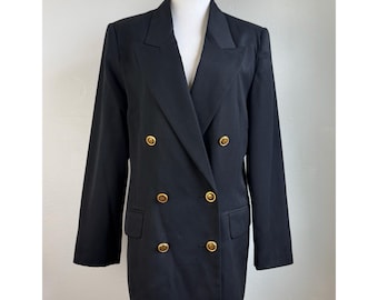 May include: A black double-breasted blazer featuring long sleeves, notched lapels, and six gold-toned metal buttons arranged in two vertical rows. The garment includes two front flap pockets and is displayed on a mannequin torso.