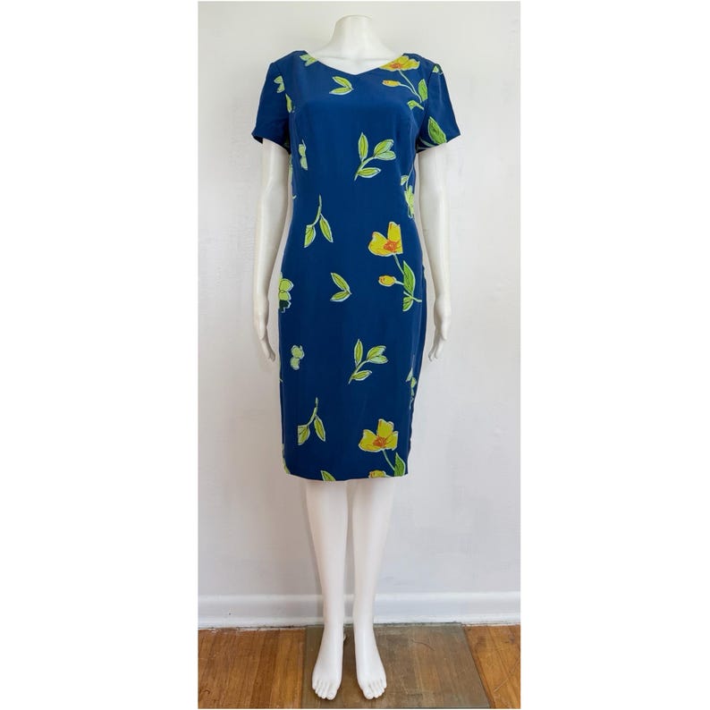 Puede incluir: Vestido azul marino con estampado floral. El vestido tiene cuello en V y mangas cortas. Flores amarillas y hojas verdes adornan la tela. El vestido llega a la rodilla y es entallado.