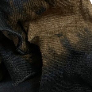 May include: Close-up of a brown and black fabric with a tie-dye pattern. The fabric is soft and textured, with a subtle sheen.