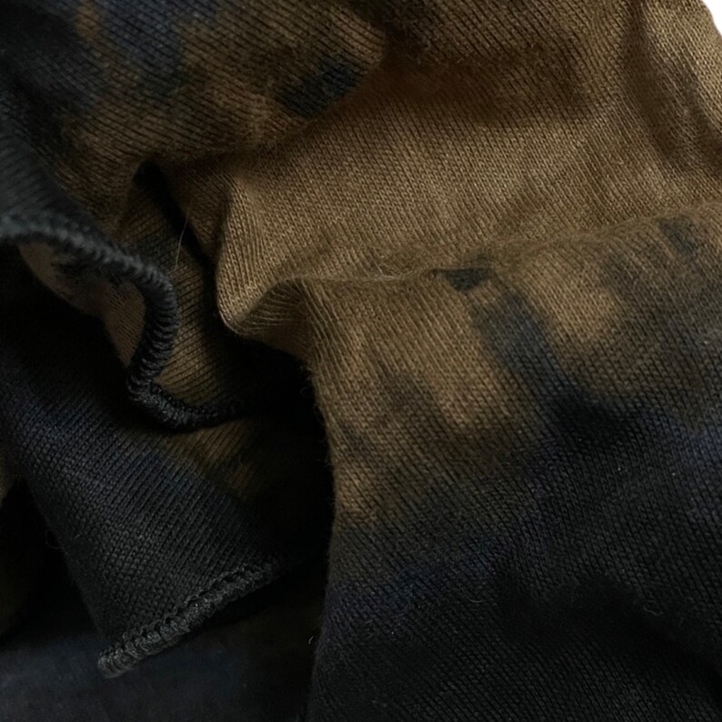 May include: Close-up of a brown and black fabric with a tie-dye pattern. The fabric is soft and textured, with a subtle sheen.