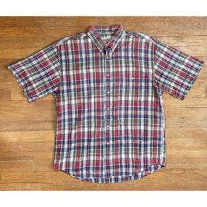 May include: A short-sleeved button-down shirt with a plaid pattern in shades of red, green, blue, and yellow. The shirt has a collar, a chest pocket, and a button-up front. The shirt is made of a lightweight fabric.