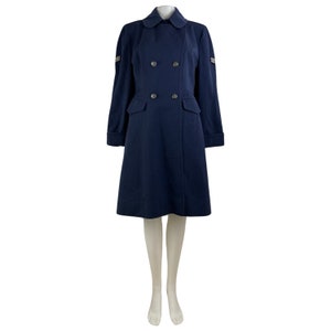 Pu&ograve; includere: Un cappotto blu navy doppiopetto con colletto e due tasche. Il cappotto ha bottoni argentati e strisce argentate sulle maniche.