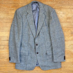 Può includere: Un blazer azzurro chiaro con un sottile motivo a quadri. La giacca presenta due tasche anteriori, una chiusura a due bottoni e tre bottoni su ogni polsino. La fodera interna è di colore azzurro chiaro.