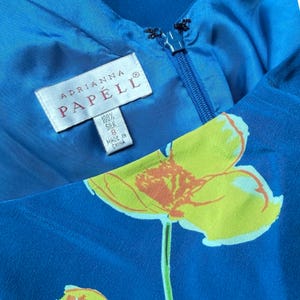 Puede incluir: Primer plano de un vestido de seda azul con un estampado floral. El vestido tiene una cremallera y una etiqueta que dice "Adrianna Papell 100% Seda, Talla 8, Hecho en China."