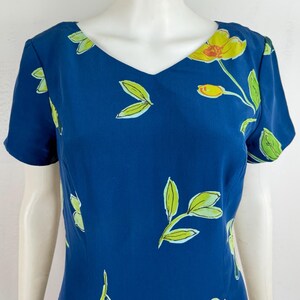 Puede incluir: Vestido azul marino con cuello en V y mangas cortas. El vestido est&aacute; adornado con un estampado floral con flores amarillas y hojas verdes. El dise&ntilde;o floral est&aacute; disperso por la tela.