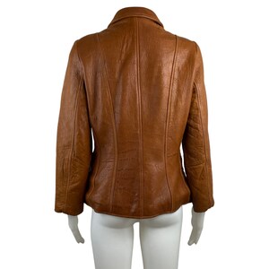 May include: A brown leather jacket with a zip fastening and a collar. The jacket has a textured surface and a fitted silhouette.