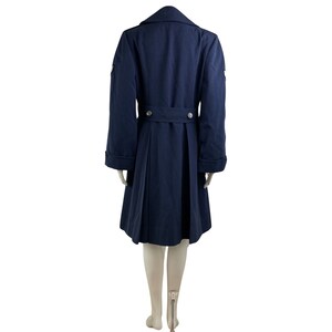 Pu&ograve; includere: Un cappotto blu navy doppiopetto con cintura e due tasche sul davanti. Il cappotto ha un colletto e maniche lunghe con polsini.