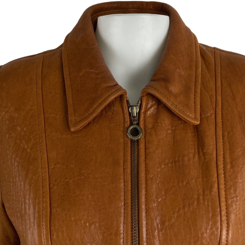 May include: A brown leather jacket with a zip fastening. The jacket has a collar and a textured surface.
