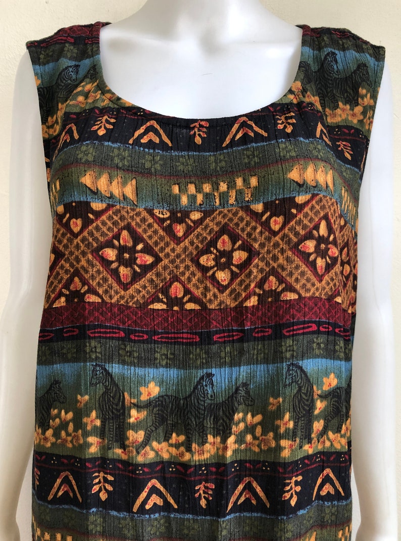 May include: A sleeveless, multi-colored dress with a geometric pattern featuring zebras, flowers, and abstract shapes. The dress is made of a soft, textured fabric.
