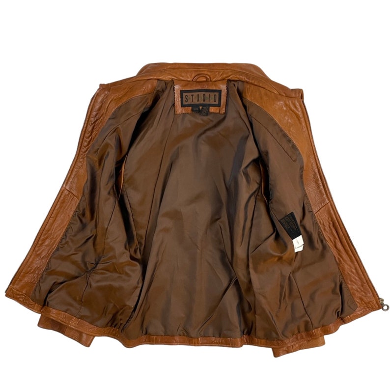May include: Brown leather jacket with a zip fastening and a STUDIO label on the inside. The jacket is unbuttoned and turned inside out, revealing the brown lining.