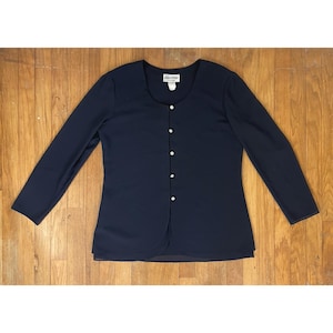 May include: A navy blue long-sleeved button-up blouse with a round neckline. The blouse has a layered look and features silver buttons down the front.