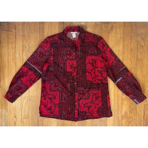 May include: A red button-up shirt with a black and gray paisley print. The shirt has long sleeves and a collared neckline.
