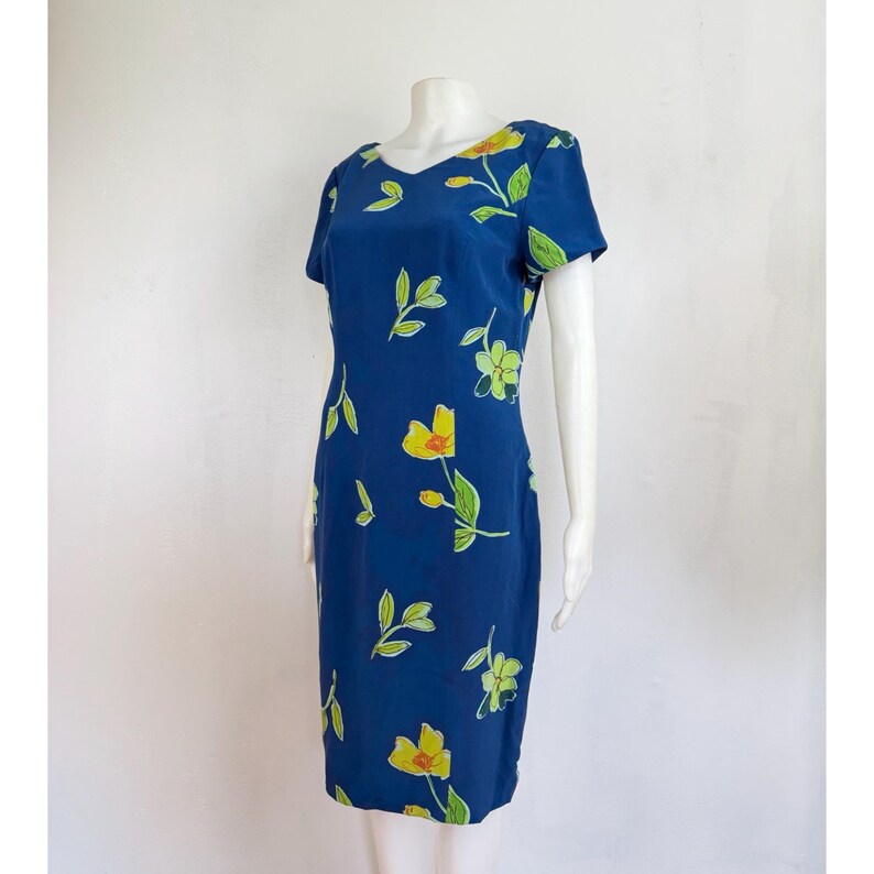 Puede incluir: Un vestido azul marino con cuello en V y mangas cortas. El vestido est&aacute; adornado con un estampado floral con flores amarillas y hojas verdes. El vestido se exhibe en un maniqu&iacute;.