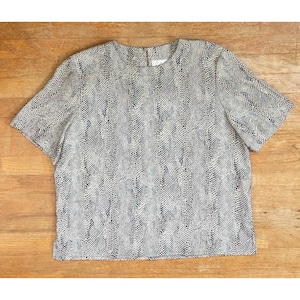 Könnte beinhalten: Eine kurzärmlige Bluse mit Schlangenmuster in Beige-, Grau- und Schwarztönen. Das Oberteil hat einen runden Ausschnitt und einen kleinen Reißverschluss hinten. Der Stoff scheint leicht zu sein.