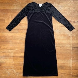 May include: A black velvet dress with long sleeves. The sleeves and upper bodice feature a textured, leaf-like pattern. The dress has a scoop neckline and a long, straight skirt.