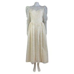 May include: A white lace wedding dress with a sweetheart neckline and puff sleeves. The dress has a fitted bodice and a full skirt.