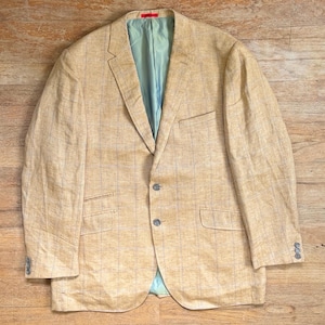 May include: A tan blazer featuring a subtle light blue windowpane check pattern. The jacket has a notched lapel, two front buttons, two flap pockets, a chest pocket, and a light blue interior lining. The sleeves are finished with three buttons.